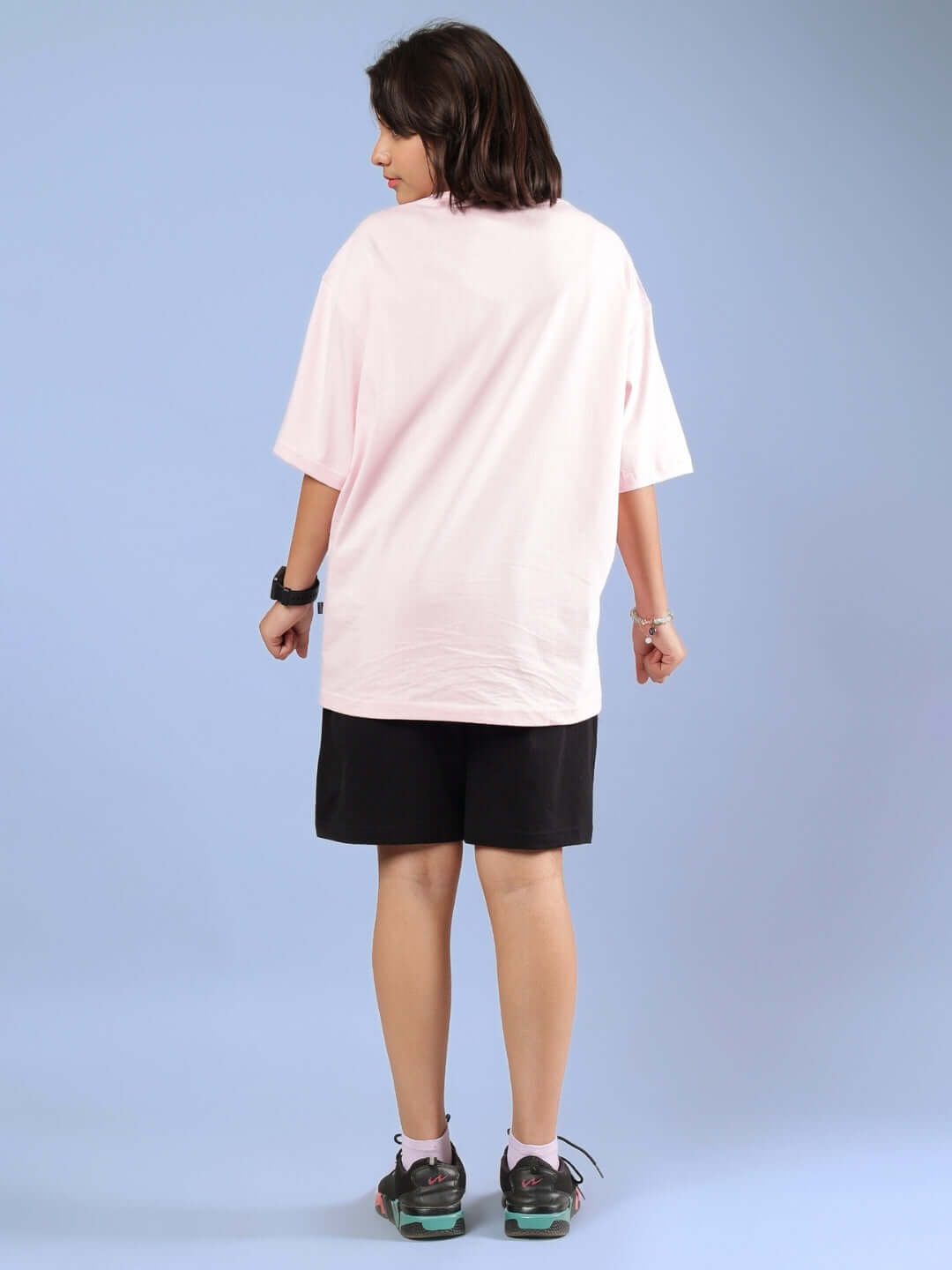 Child wearing BE KIND CO-ORD FOR BOYS GIRLS PINK-BLACK outfit from behind, featuring a pink tee and black shorts, on a light blue background.