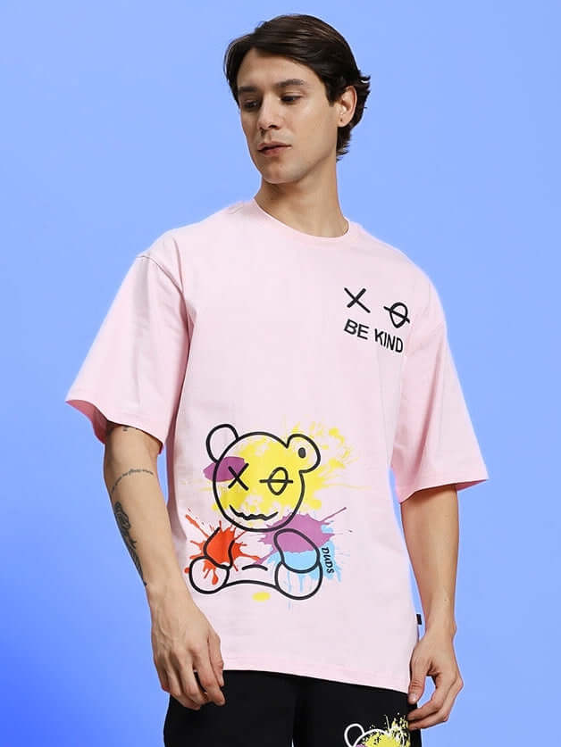 Man wearing BE KIND OVER-SIZED T-SHIRT PINK with graphic design, set against a light blue background.