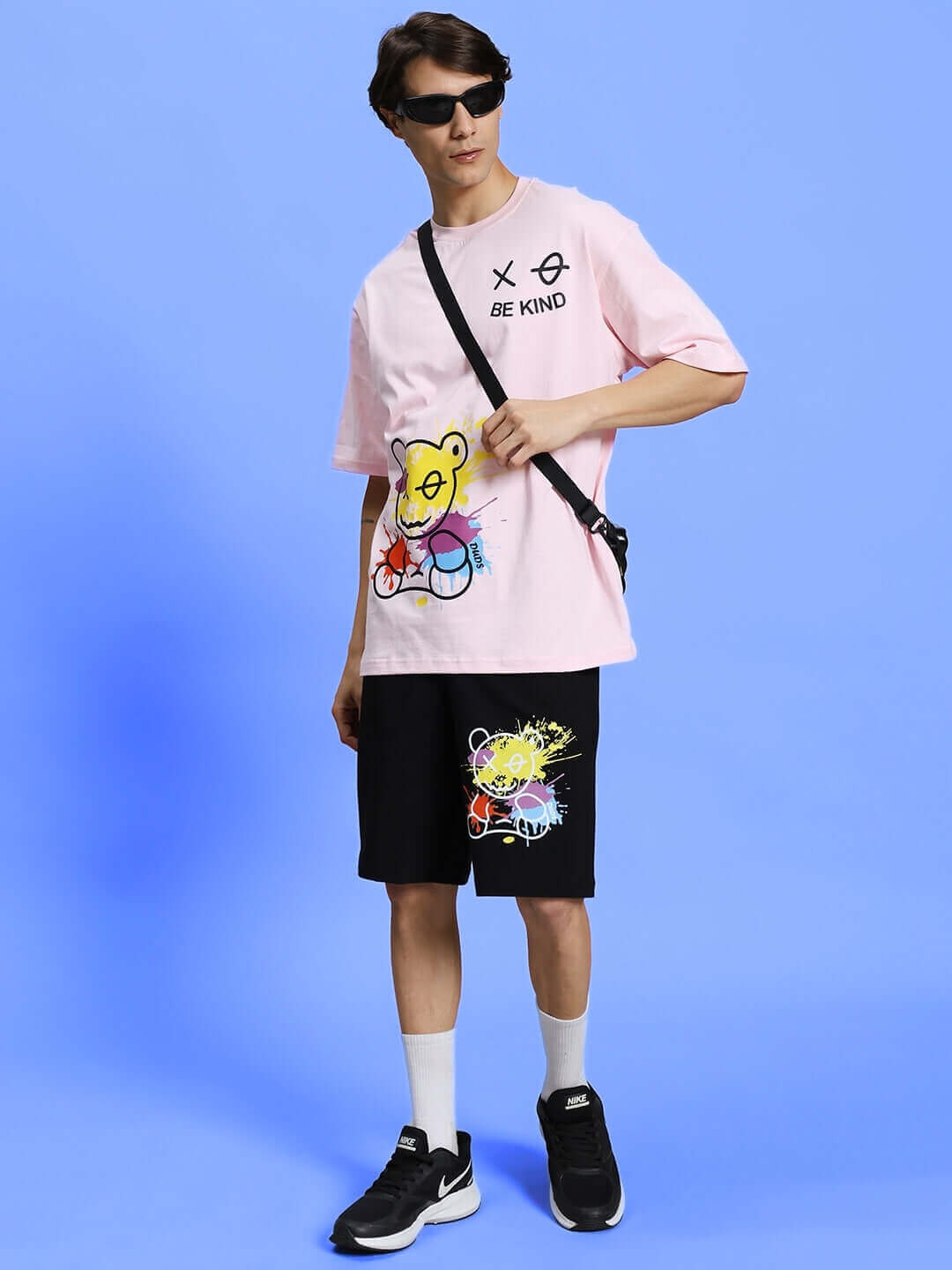 Model wearing BE KIND REGULAR FIT SHORTS BLACK with graphic tee and accessories against blue background