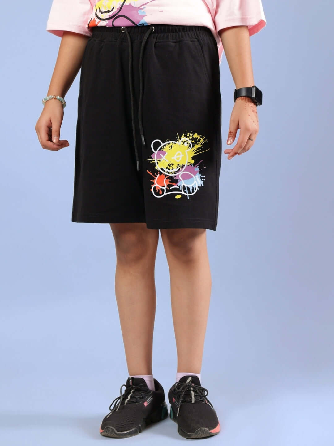 Child wearing BE KIND SHORTS FOR BOYS & GIRLS BLACK with colorful design, standing against a blue background, showing comfort and style.