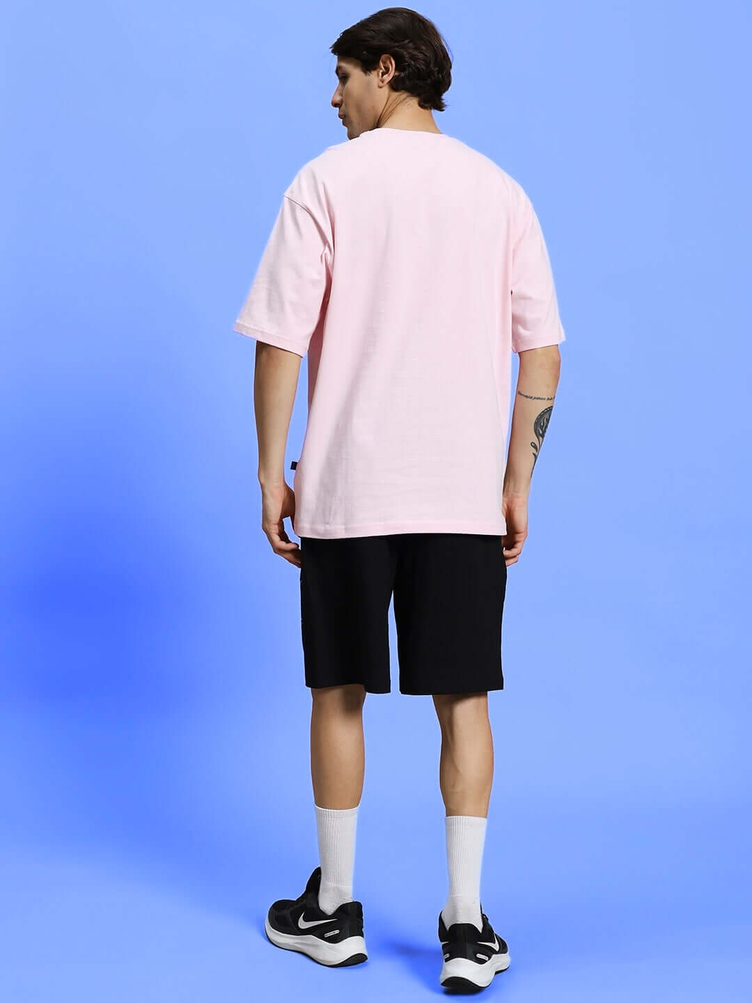 Model wearing BE KIND SUMMER CO-ORD SET PINK-BLACK with pink t-shirt and black shorts, back view on blue background.