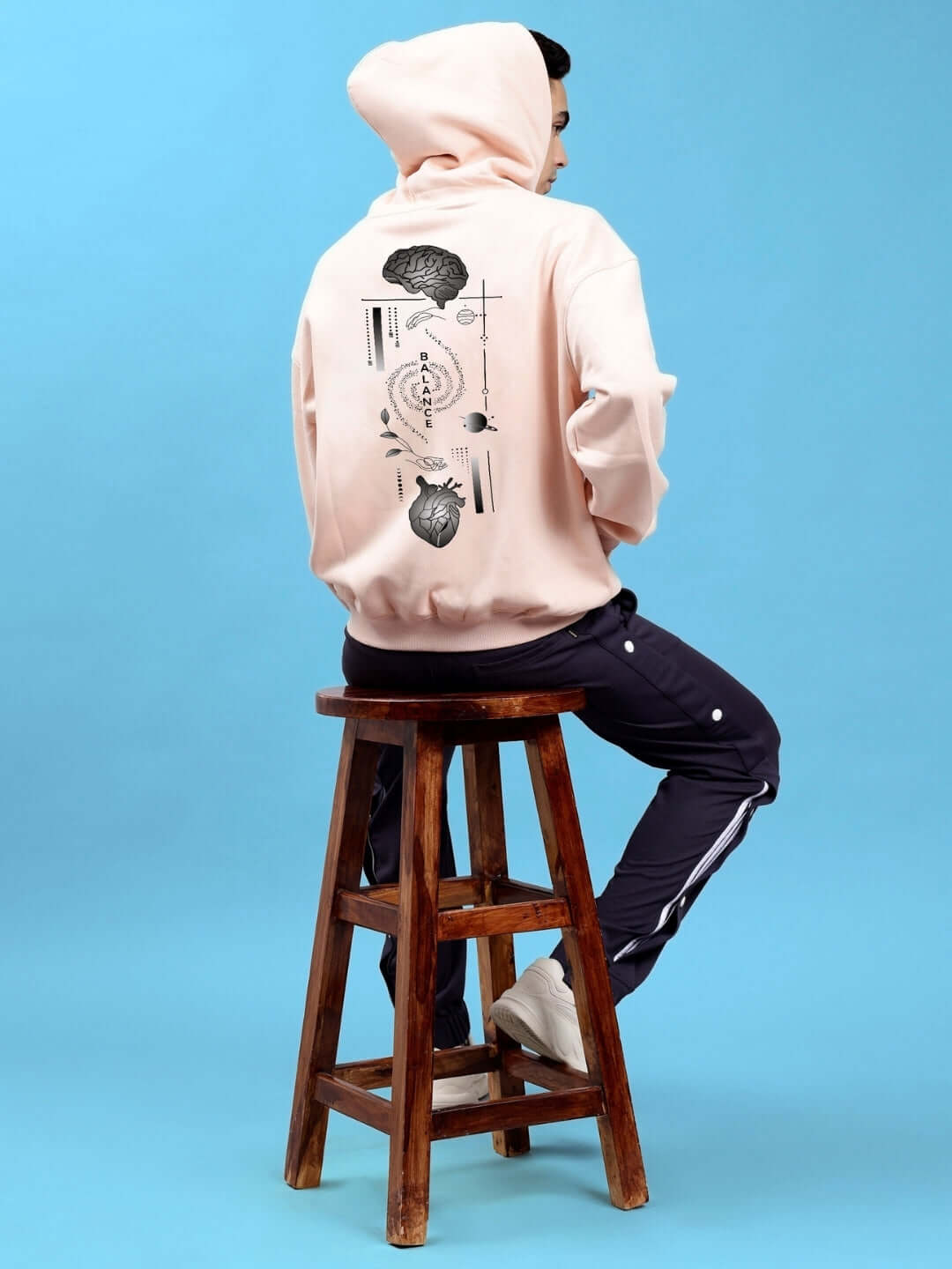 Person wearing BALANCE OVER-SIZED FLEECE HOODIES BEIGE sitting on a stool, showcasing back design.