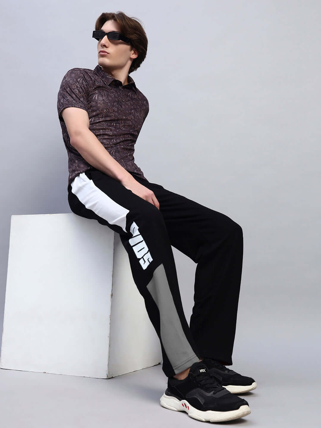 Man wearing BELGIANS Relaxed-Fit Joggers in black grey, seated stylishly with DUDS branding, showcasing casual fashion and comfort.
