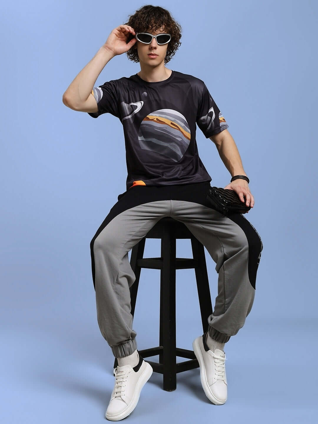Model wearing BERLIN RELAXED FIT JOGGERS BLACK GREY seated on stool, showcasing style and comfort in sporty outfit.