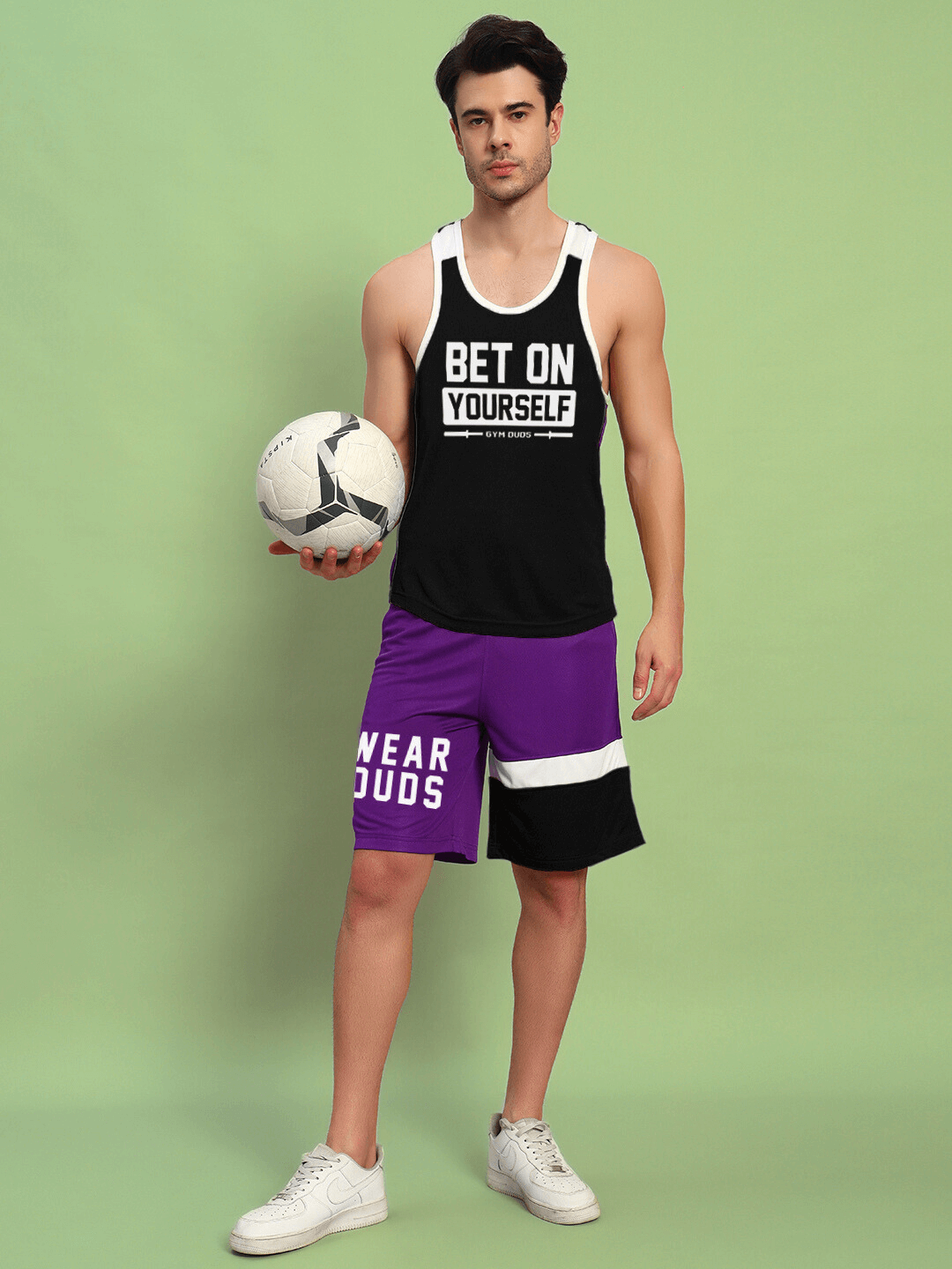 Man wearing BET ON YOURSELF GYM CO-ORD SET BLACK PURPLE holding soccer ball, showcasing fitness apparel.