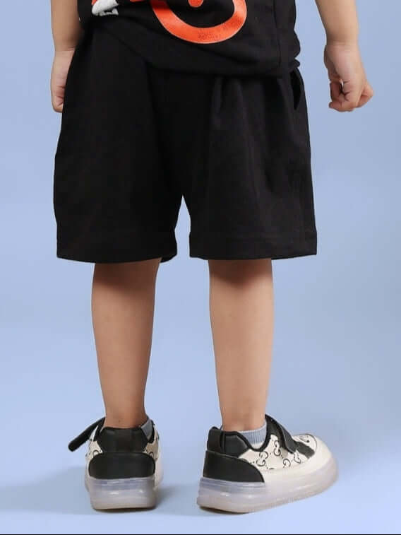 Child wearing BINGO SHORTS FOR BOYS & GIRLS BLACK, showcasing rear view and casual sneakers on a blue background.