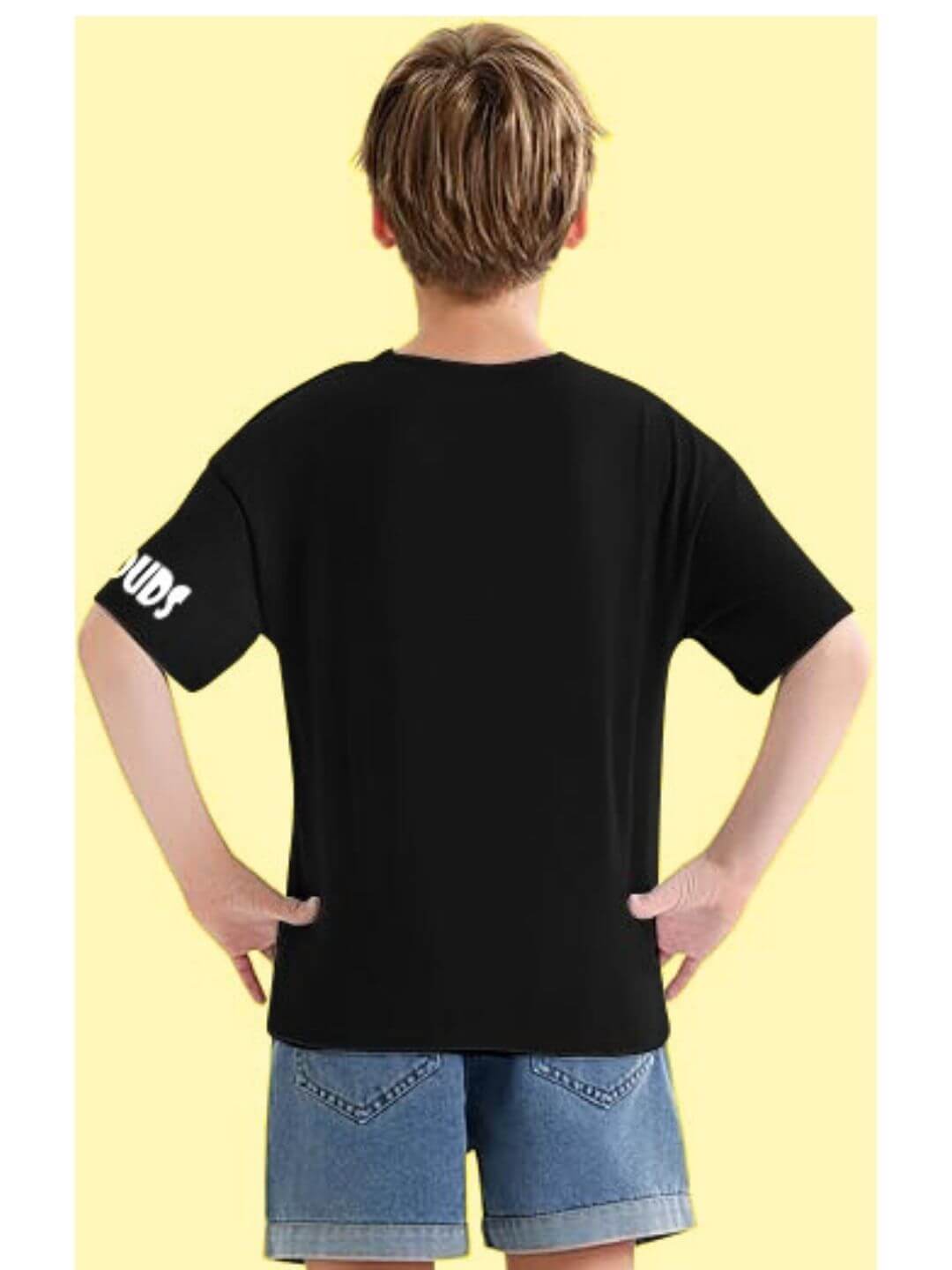 Back view of child in DUCK FACE T-SHIRT FOR BOYS AND GIRLS BLACK, wearing denim shorts, standing with hands on hips.