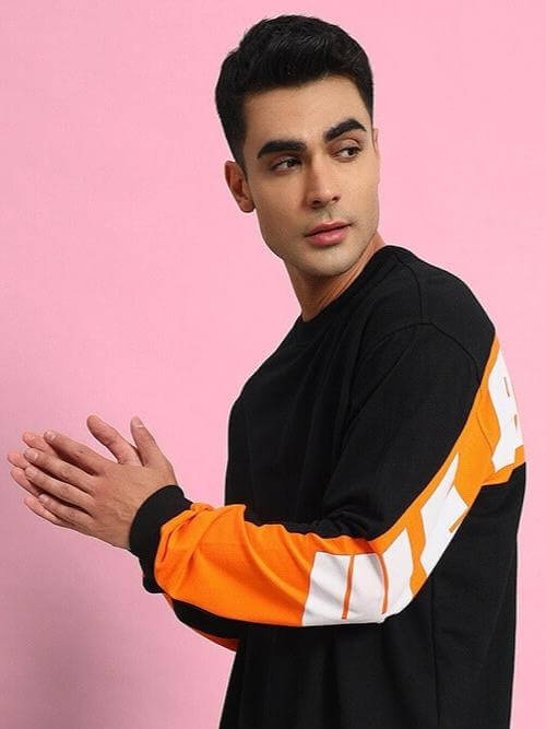Model wearing black oversized co-ord set with orange and white contrast sleeves, standing against pink background.