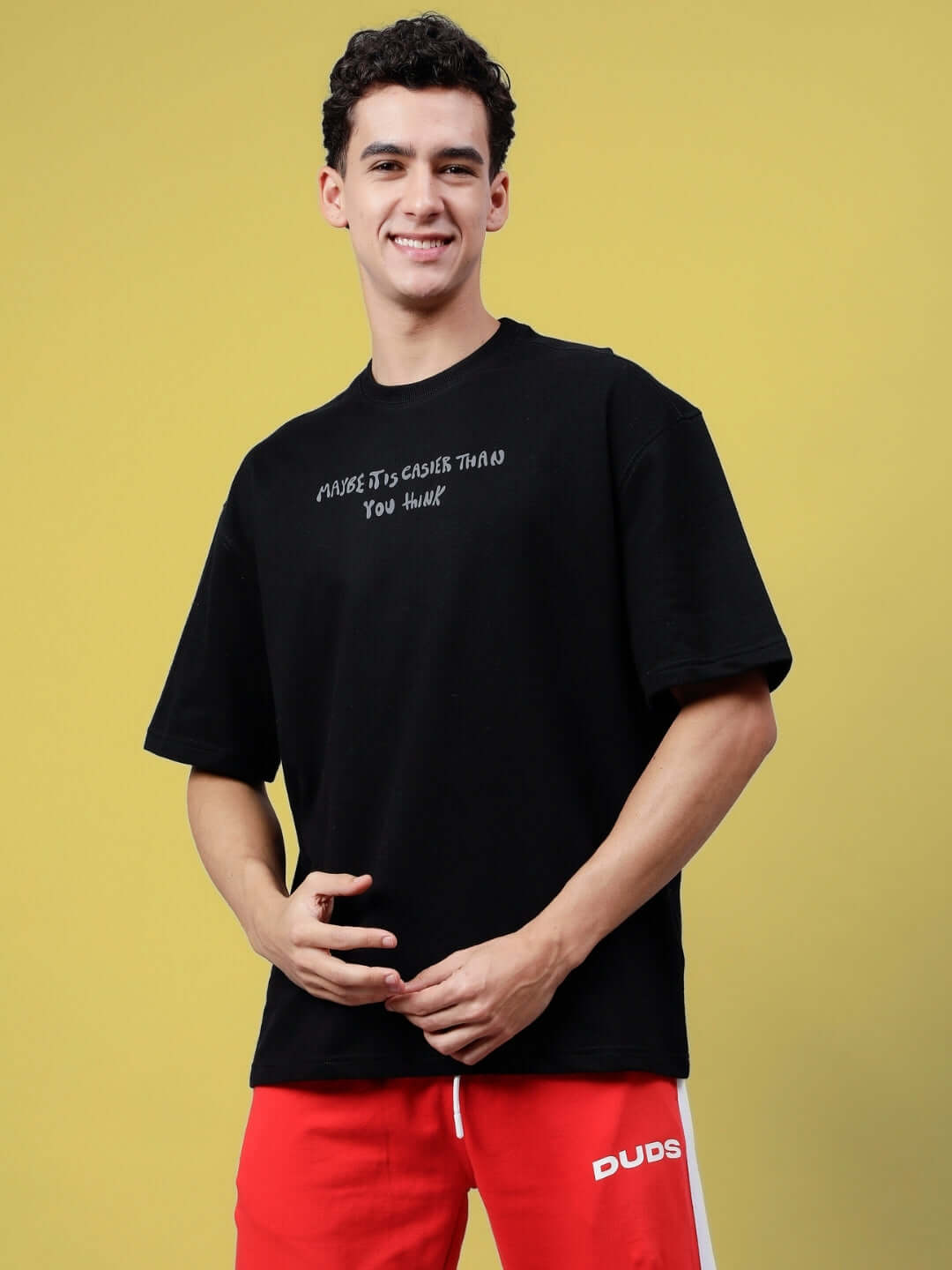 Man smiling wearing MAYBE IT IS EASIER THAN YOU THINK REFLECTOR T-SHIRT BLACK against a yellow background