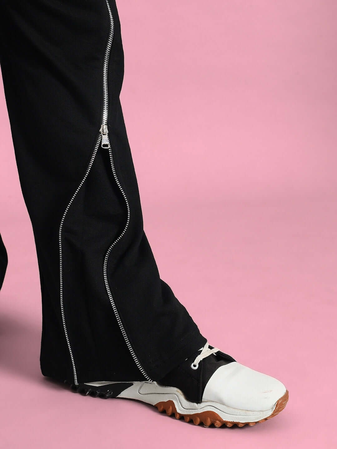 Black slider joggers with zipper detail and white sneaker on a pink background.
