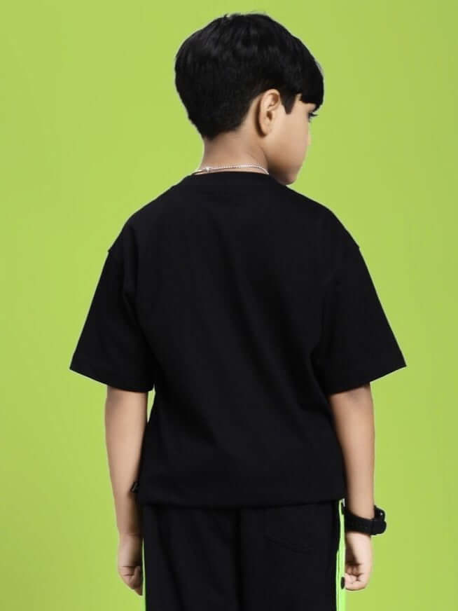Child wearing the WOODY BUZZ T-SHIRT FOR BOYS AND GIRLS BLACK showing back view against green background