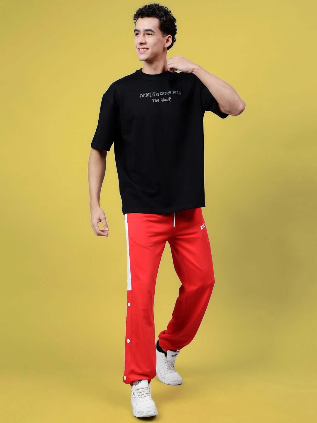 Person wearing MAYBE IT IS EASIER THAN YOU THINK REFLECTOR T-SHIRT BLACK with red pants on a yellow background, exuding confidence.