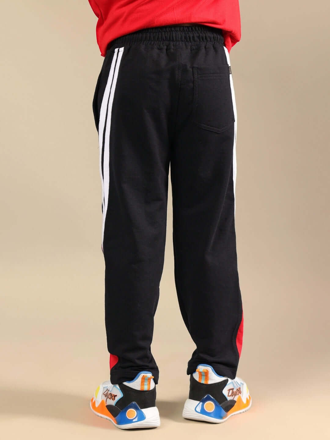 Back view of a child wearing TORNADO JOGGER FOR BOYS & GIRLS BLACK, showcasing sporty style with white stripes and red accents.