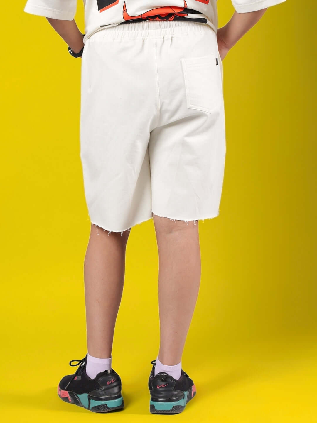 Child wearing BLAZE BULLS SHORTS FOR BOYS & GIRLS OFF-WHITE, showcasing rear view against yellow background