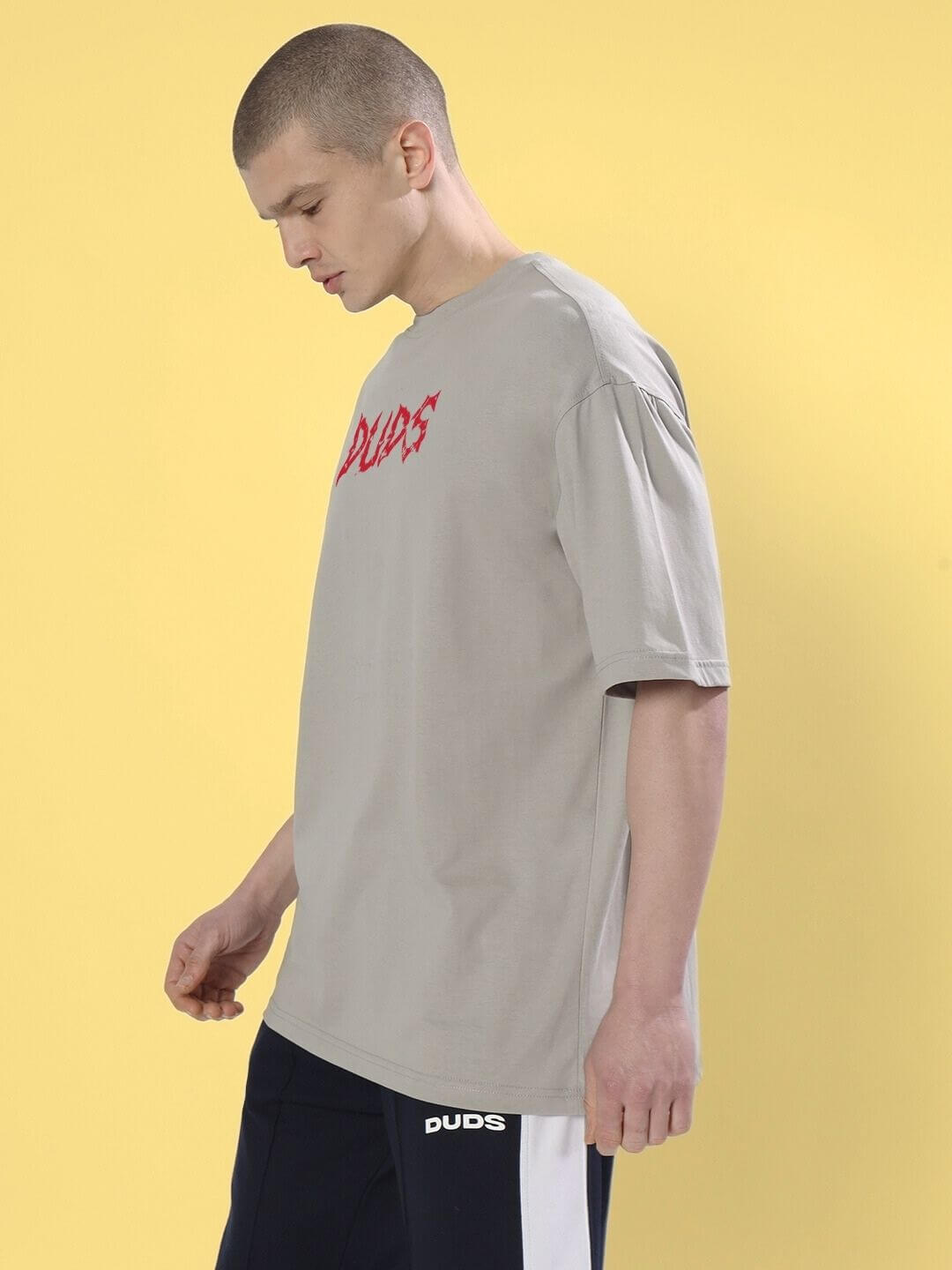 Model wearing BLOODY EYE OVER-SIZED T-SHIRT GREY, showcasing the bold red graphic on a soft grey backdrop, styled with black pants.