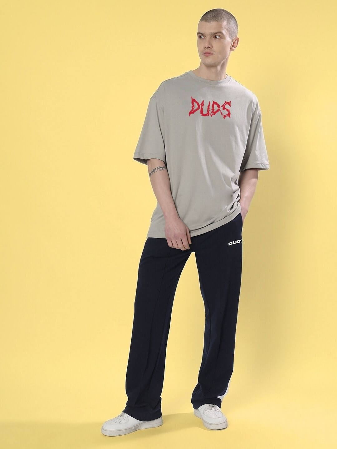 Man wearing BLOODY EYE OVER-SIZED T-SHIRT GREY with graphic design, styled with black pants and white sneakers, against a yellow background.