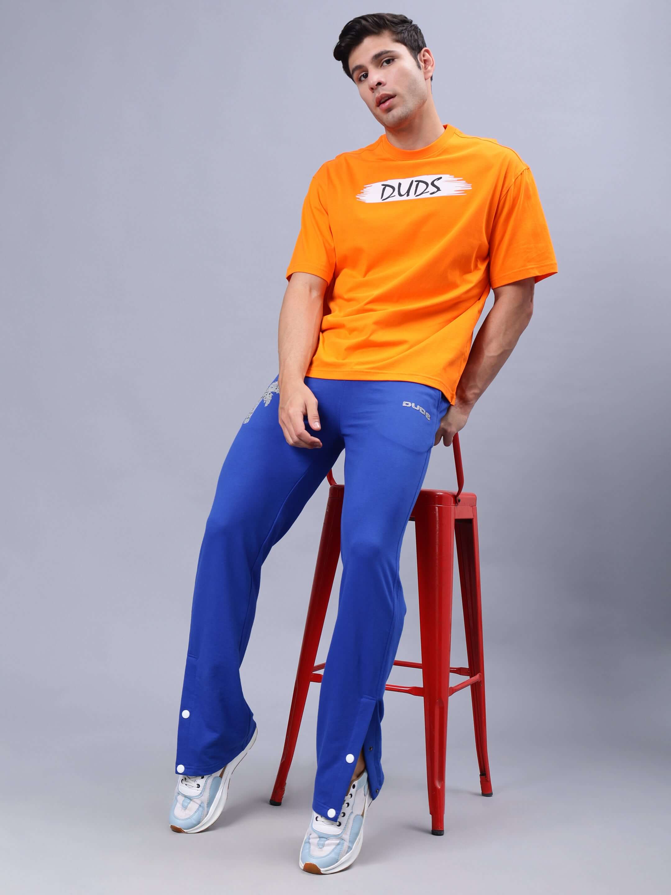 Model wearing BLOOM QUOTE OVER-SIZED T-SHIRT in orange with blue pants, promoting the customizable fit option by DUDS.