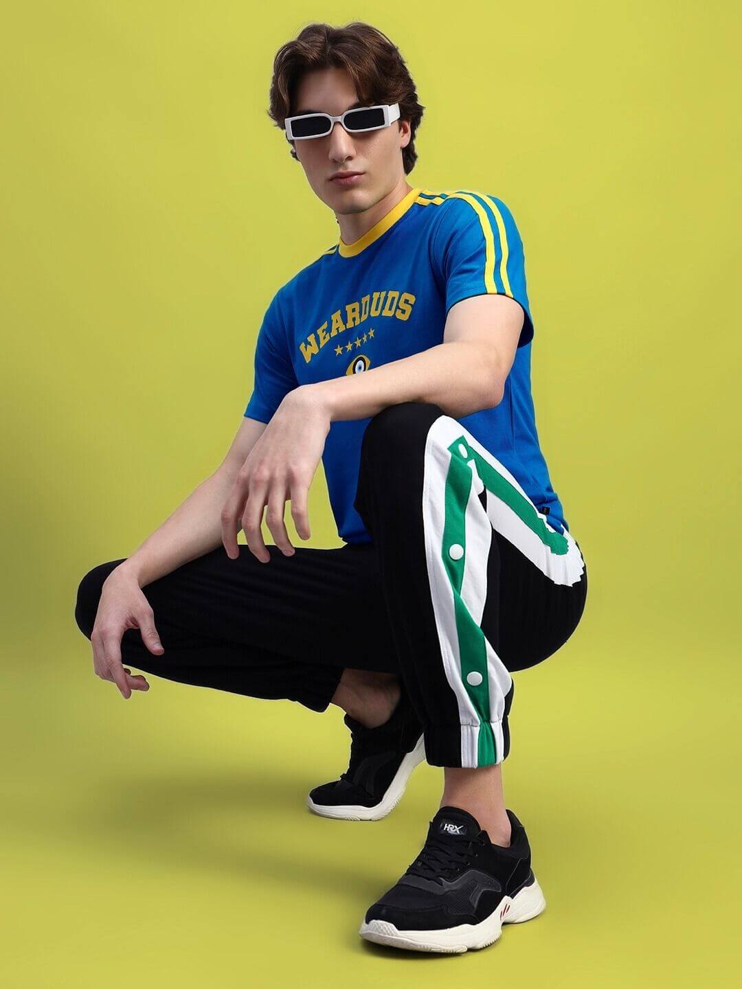 Model wearing blue Irish regular fit t-shirt and black athletic pants with stripes, posing against a yellow background.