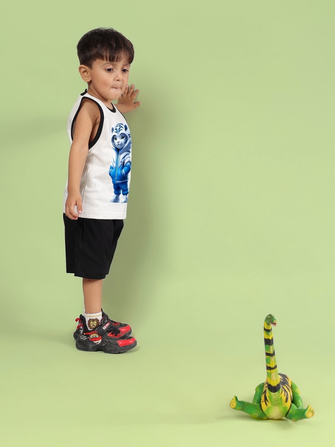 Child in white and black sleeveless top playing with dinosaur toy against green background