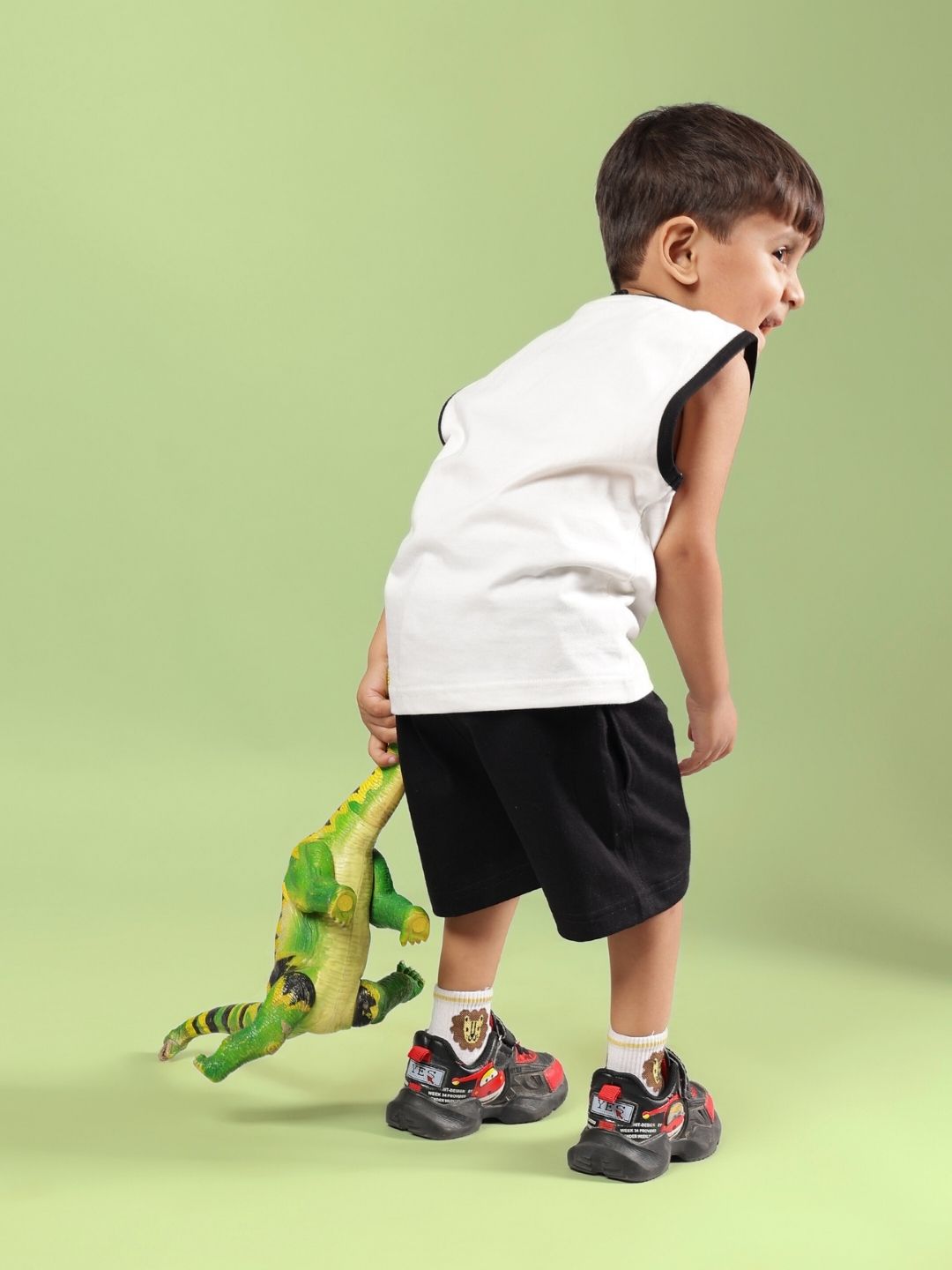 Child wearing Blue Cat summer co-ord in white and black, holding a green toy dinosaur, set against a light green background.