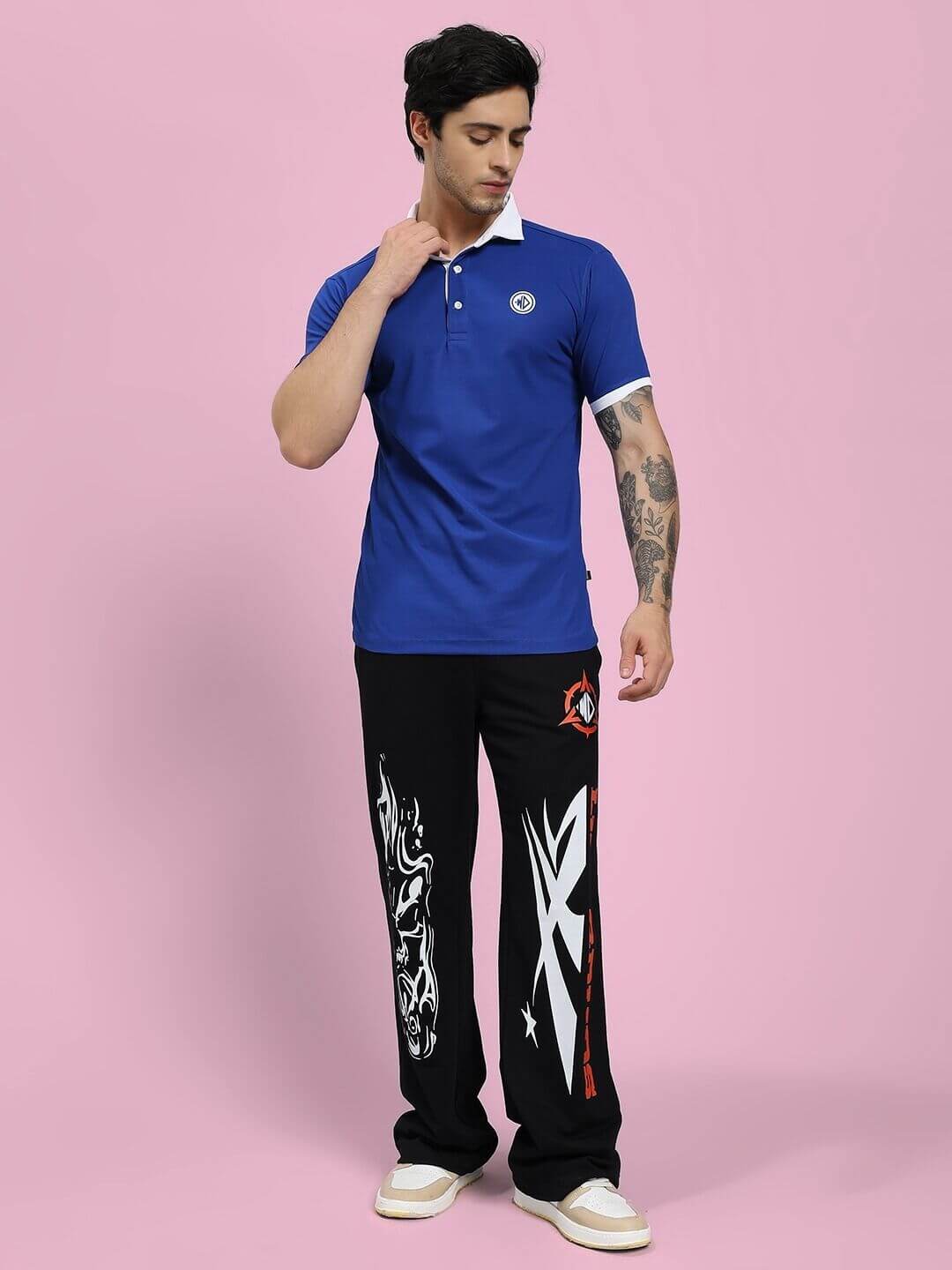 Man wearing BLUE EDGE POLO REGULAR FIT T-SHIRT BLUE with printed black pants, standing against pink background