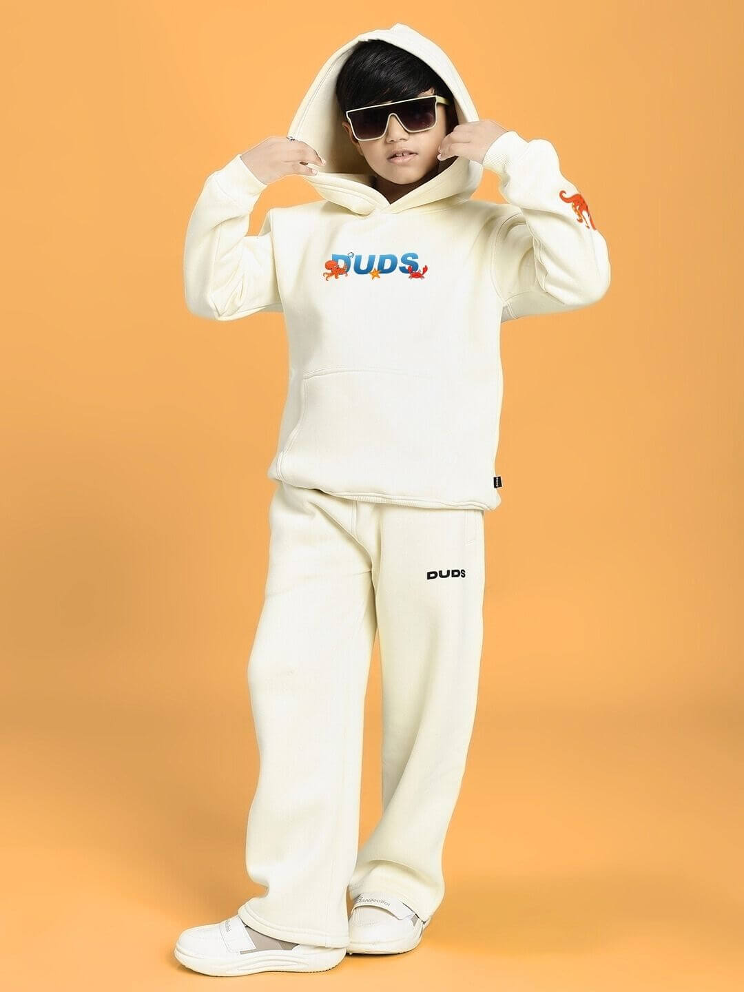 Child wearing BLUE OCEAN WORLD FLEECE CO-ORD FOR BOYS AND GIRLS OFF-WHITE in a stylish pose against an orange background.