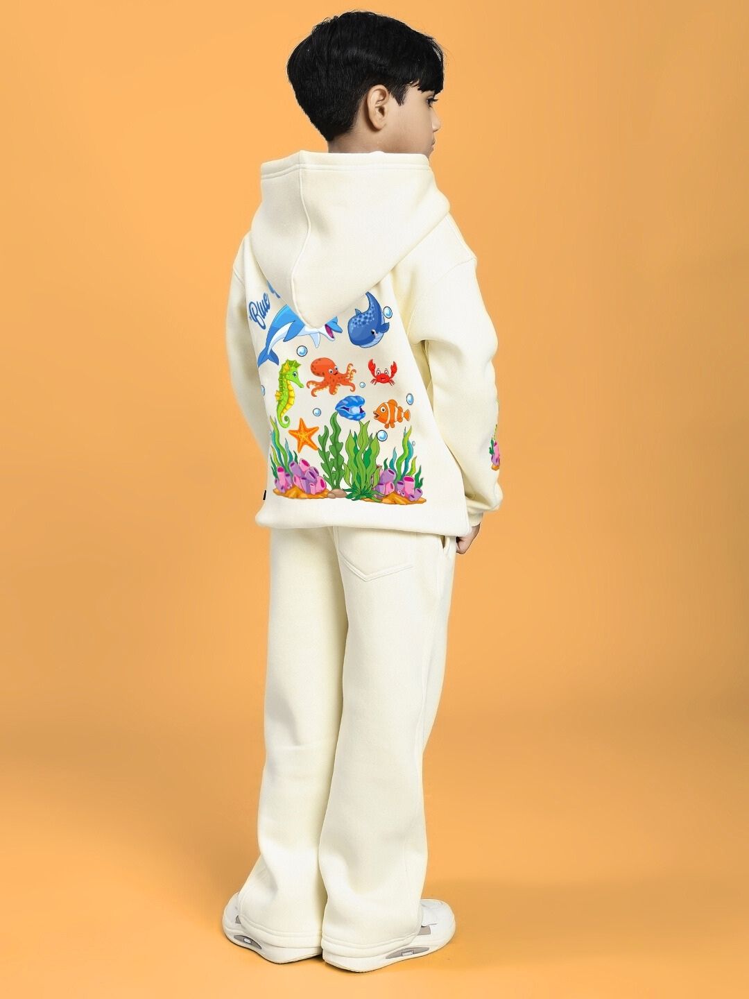 Child wearing BLUE OCEAN WORLD FLEECE CO-ORD FOR BOYS AND GIRLS OFF-WHITE set with colorful ocean design, rear view on orange background.