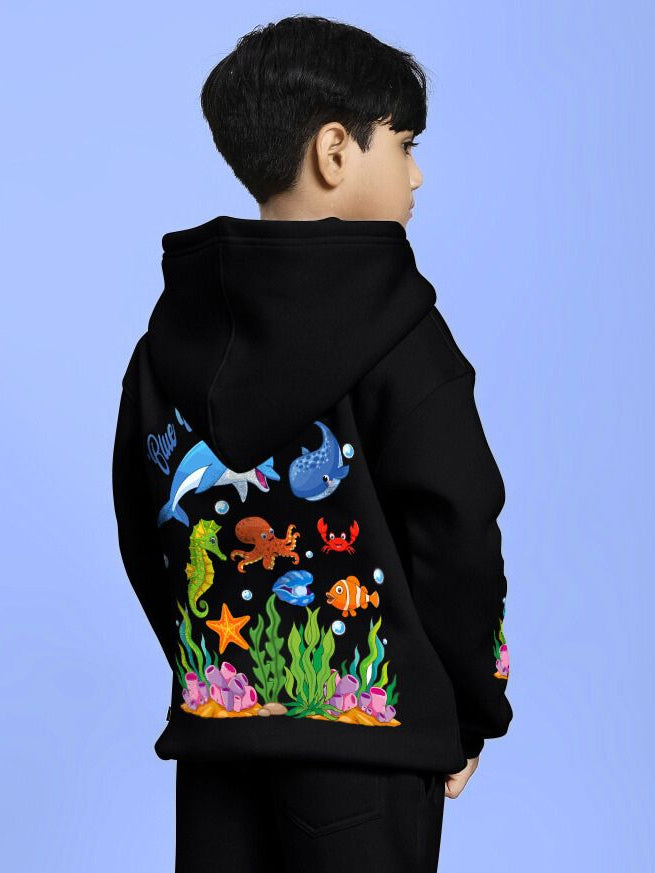 Child wearing BLUE OCEAN WORLD FLEECE HOODIE FOR BOYS AND GIRLS BLACK with ocean-themed design on the back, standing in profile.