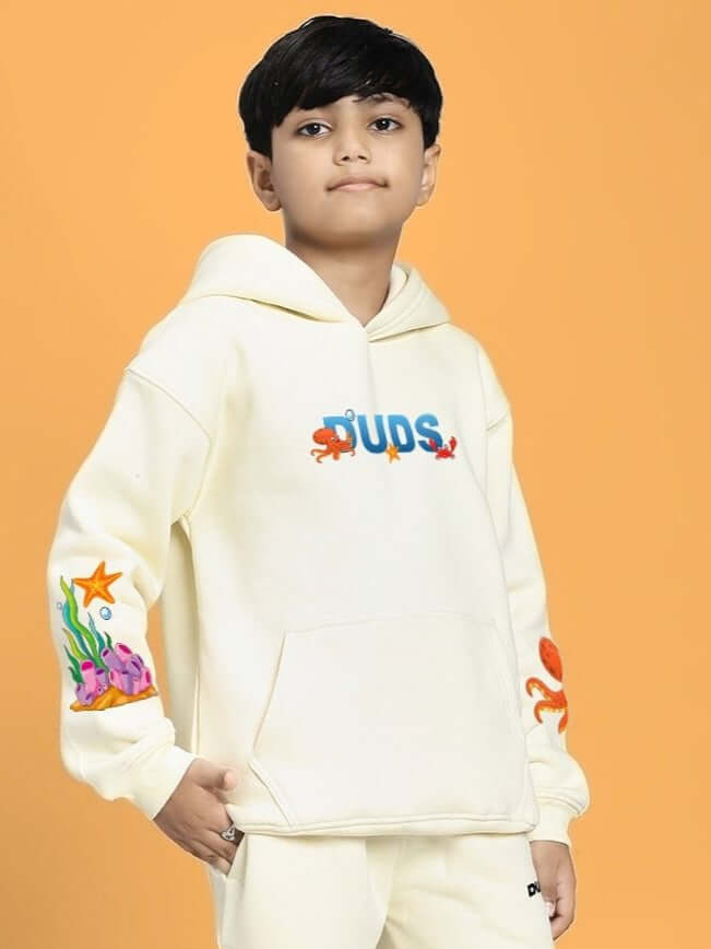 Youth wearing BLUE OCEAN WORLD FLEECE HOODIE FOR BOYS AND GIRLS OFF-WHITE with marine-themed sleeve design on orange background