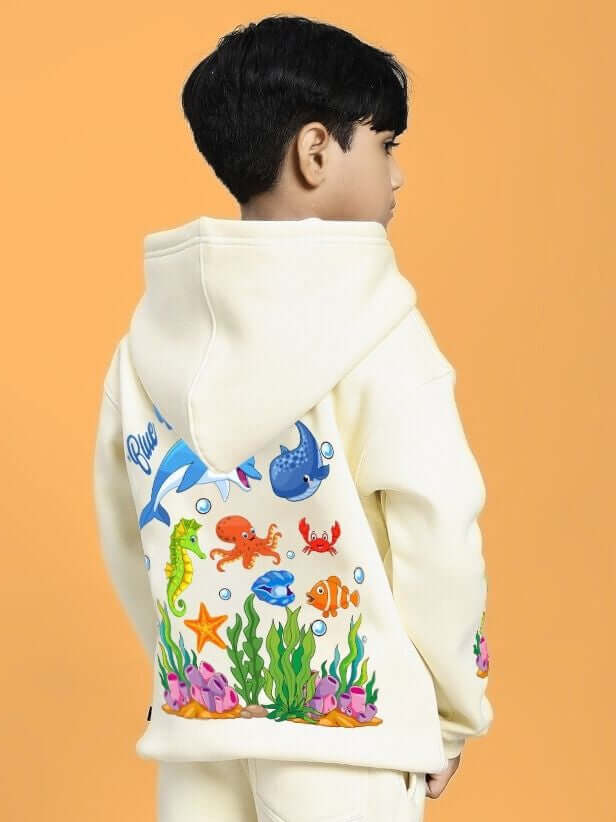 Child wearing BLUE OCEAN WORLD FLEECE HOODIE FOR BOYS AND GIRLS OFF-WHITE with ocean-themed designs.