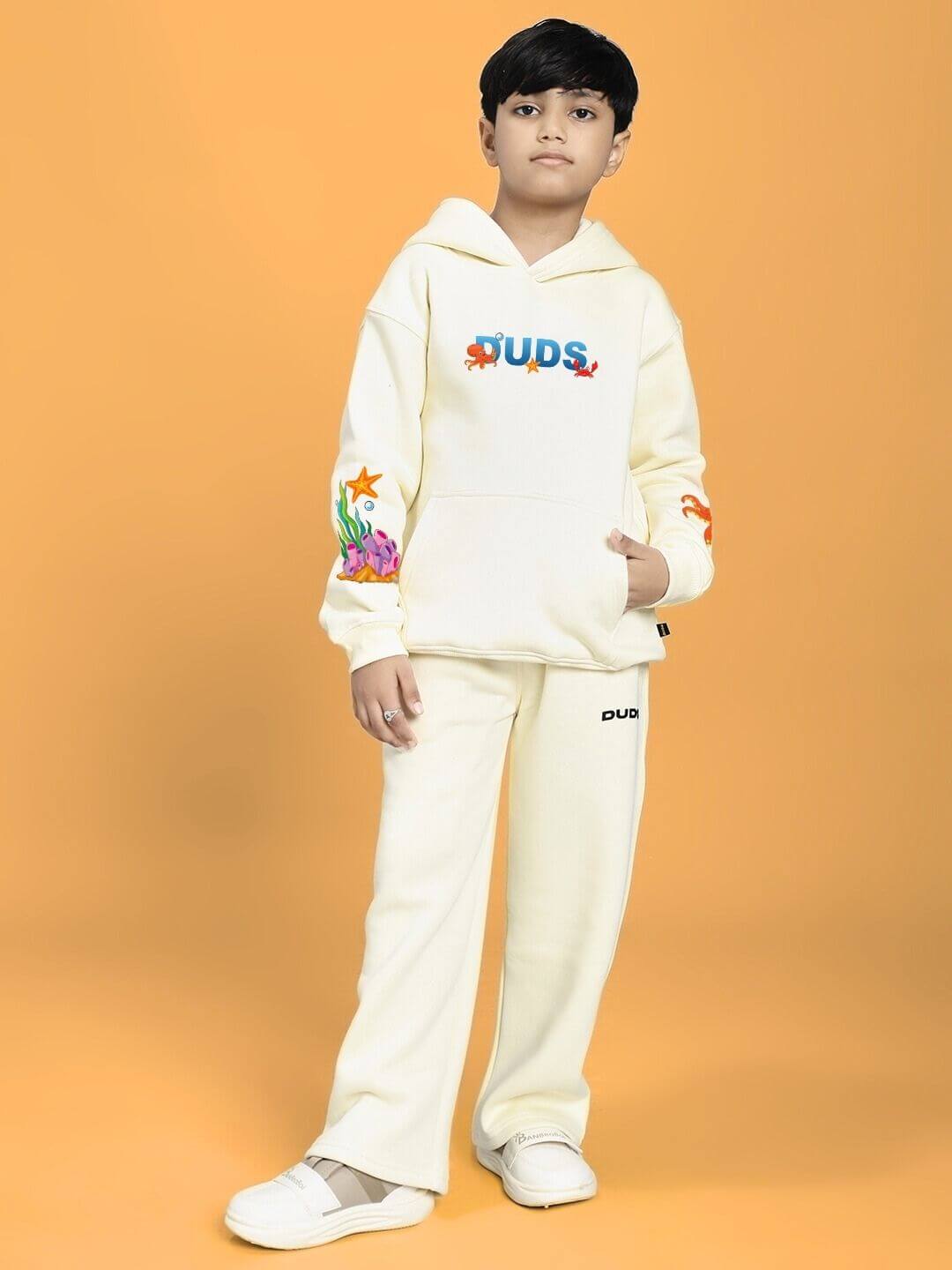 Child wearing BLUE OCEAN WORLD FLEECE CO-ORD FOR BOYS AND GIRLS OFF-WHITE against orange background.