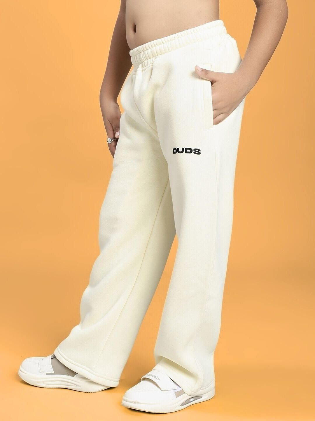 Child wearing BLUE OCEAN WORLD FLEECE JOGGER FOR BOYS AND GIRLS OFF-WHITE with hands in pockets and white sneakers.