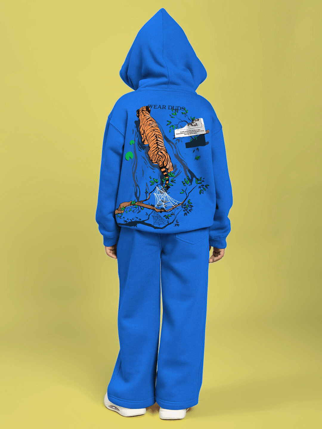 Child wearing A JOURNEY WITHIN FLEECE CO-ORD FOR BOYS AND GIRLS BLUE with tiger graphic on back, standing against a yellow background.