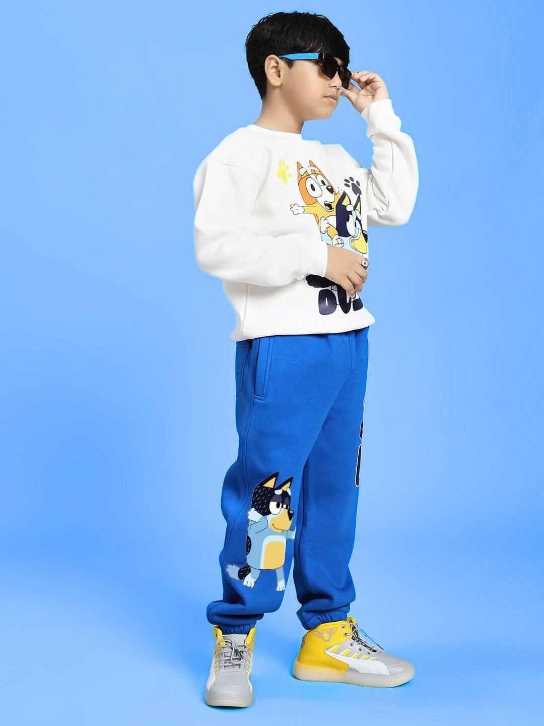 Child wearing BLUEY BINGO FLEECE JOGGER FOR BOYS AND GIRLS BLUE with character design, standing against a blue background.