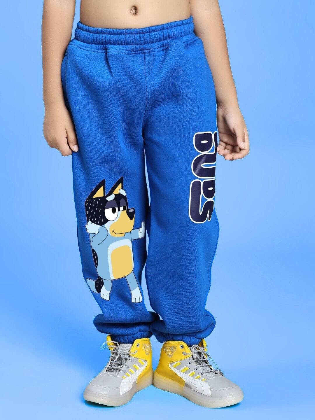 Child wearing BLUEY BINGO FLEECE CO-ORD FOR BOYS AND GIRLS WHITE BLUE pants with cartoon design on blue background.