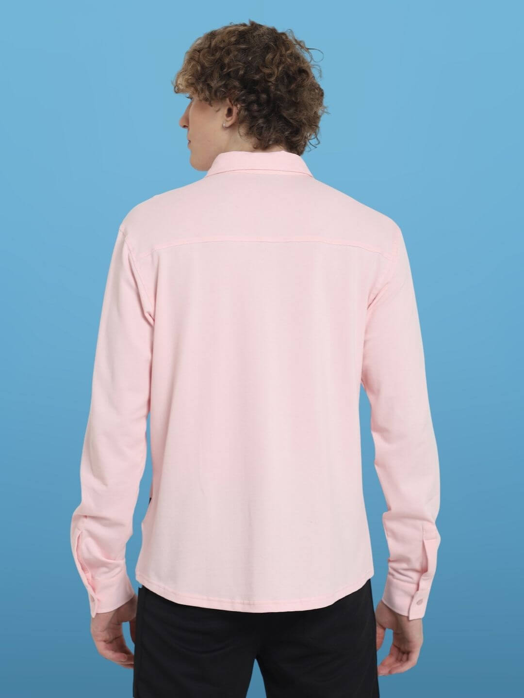 Back view of blush pink sporty pique shirt with full sleeves, wrinkle-free and 4-way stretch fabric, shown on a model against a blue background.