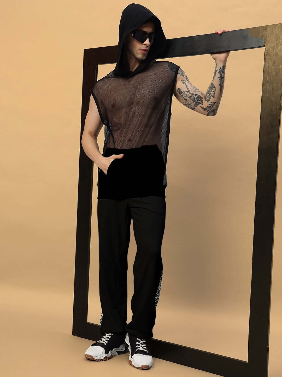 Model wearing Boogie Relaxed Fit Joggers in black, styled with a sheer mesh top and sneakers, posing with a modern frame backdrop.