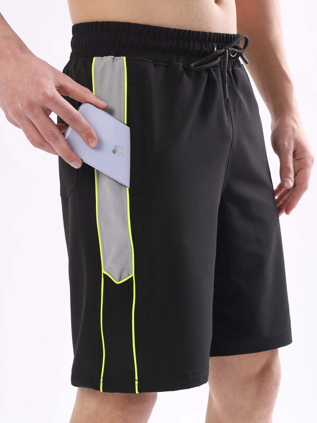 Person wearing black Boomer shorts with neon green piping, featuring a side pocket with a smartphone. Custom fit available.