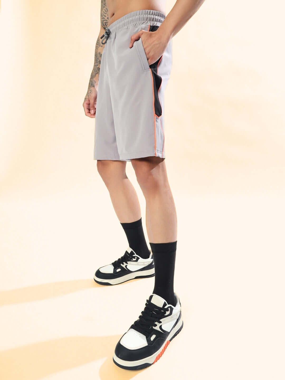 Side view of grey Boomer Shorts with orange piping, worn by a model wearing black socks and sneakers. Available in custom fit options.