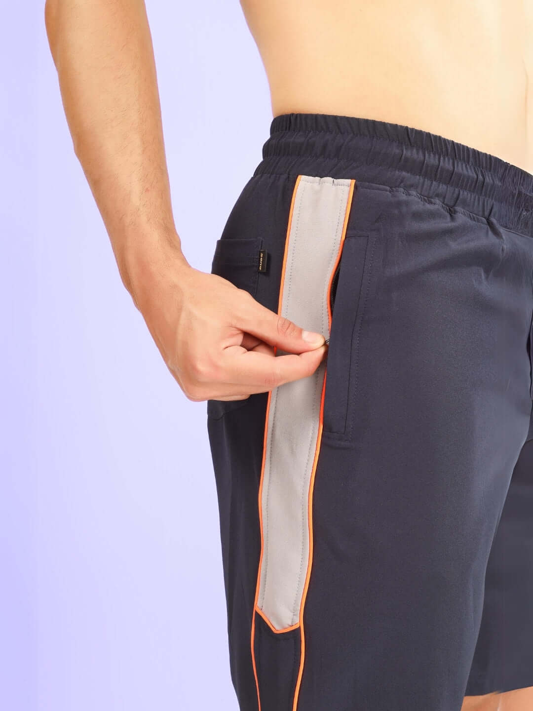 Close-up of BOOMER SHORTS NAVY WITH ORANGE PIPING showcasing side pocket and contrast piping in vibrant orange.