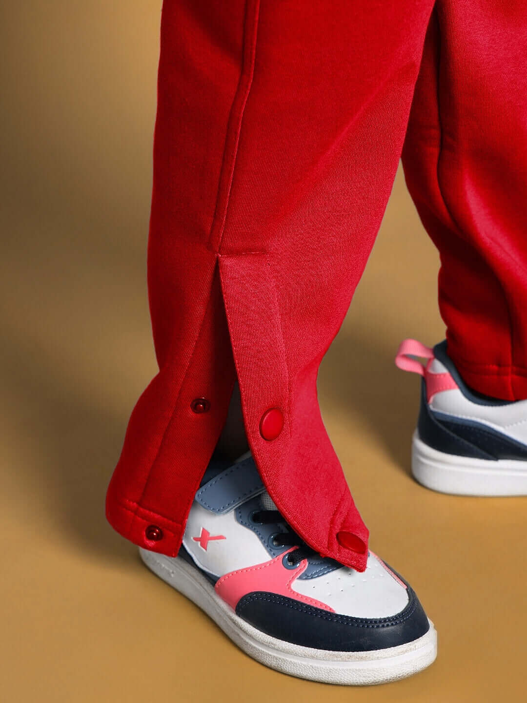 Red jogger pants for boys and girls with button detail near sneakers, "Born to Shine" edition showcasing sporty style.