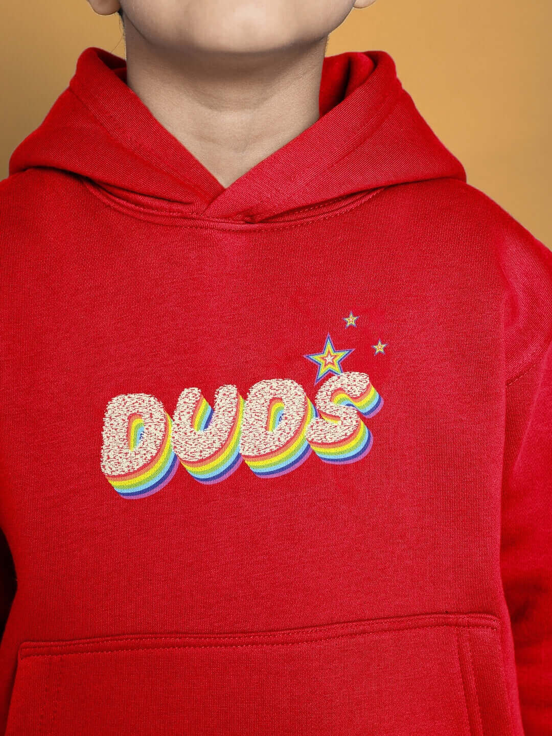 Child wearing red oversized hoodie with colorful 'DUDS' print and star design, suitable for boys and girls. "Born to Shine" collection.