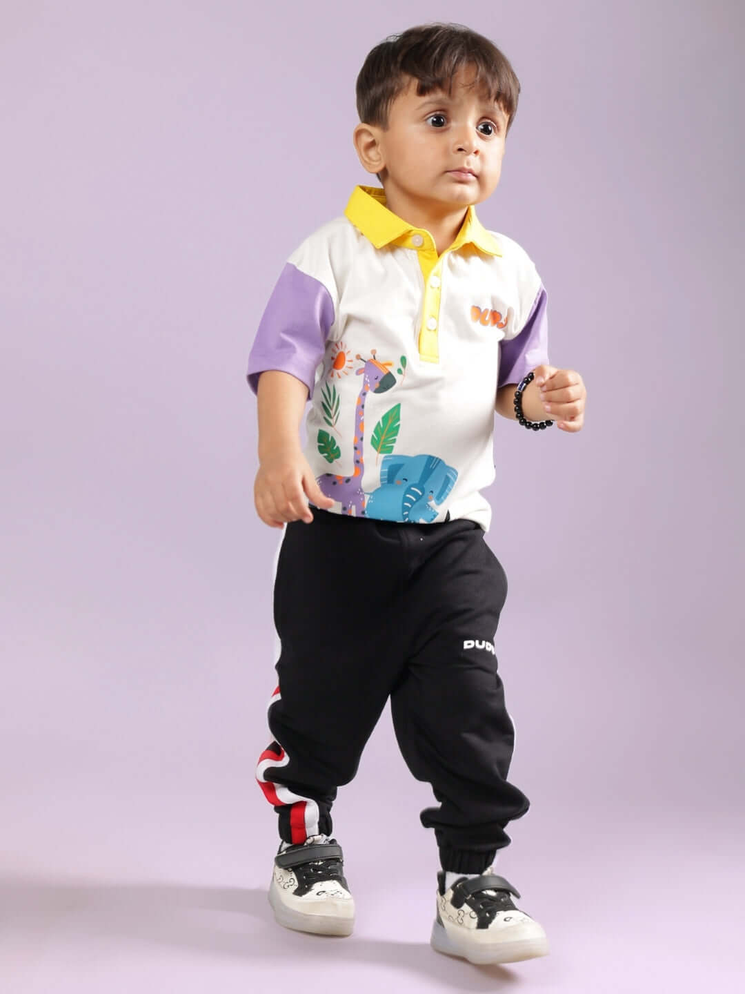 Young child modeling BORNEO CO-ORD FOR BOYS & GIRLS OFF WHITE-BLACK outfit, showcasing colorful top and black pants against a purple background.