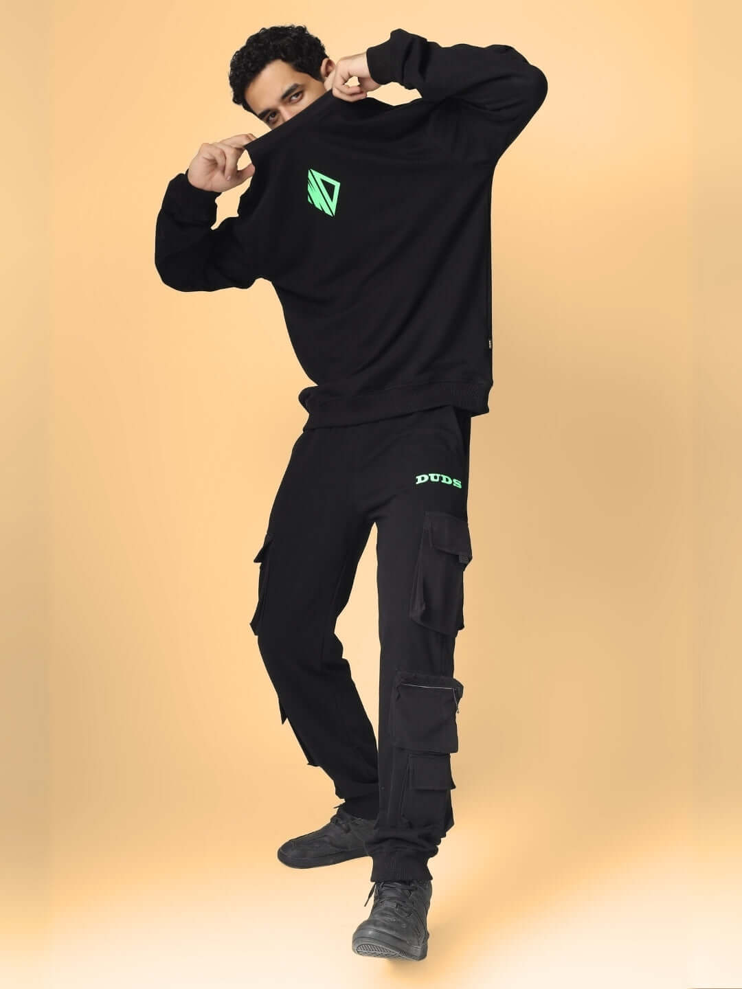 Model wearing black box pocket cargo jogger pants by DUDS against a beige background.