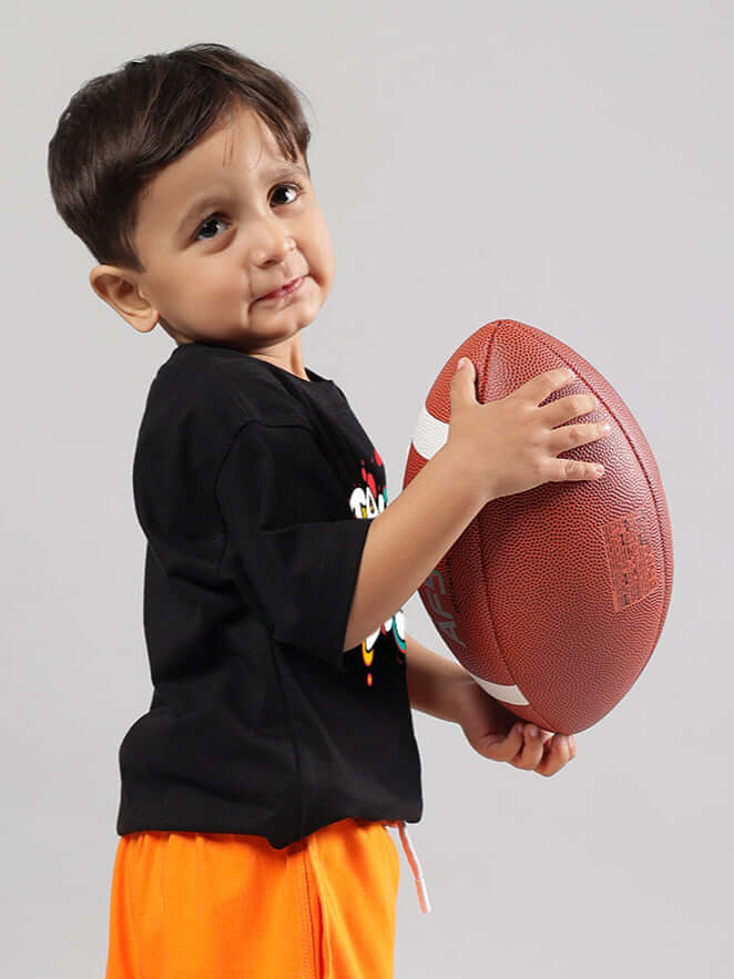 Young child wearing a black 'Take the Step' T-shirt for boys & girls, holding a football, made by DUDS.
