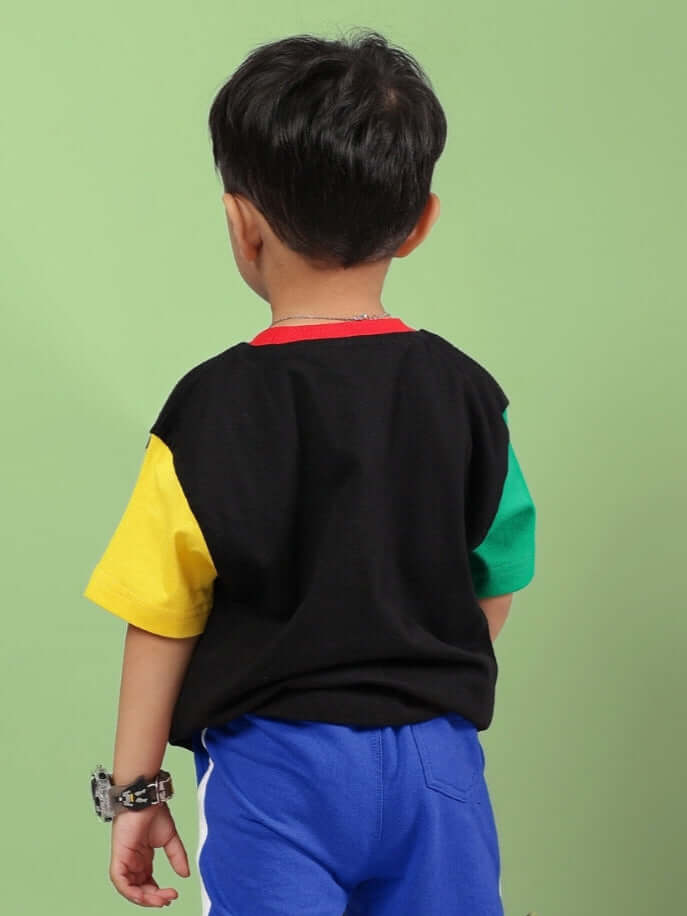 Young boy wearing PUPPY DOG PRINTRD T-SHIRT FOR BOYS GIRLS BLACK with colorful sleeves, showing back view, standing against green background.