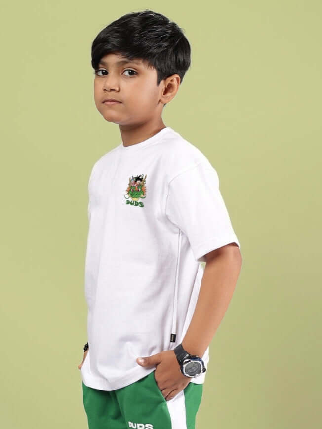 Boy wearing GOKU AND BULMA PRINTED T-SHIRT FOR BOYS GIRLS WHITE, featuring Dragon Ball Z characters, standing against a green background.