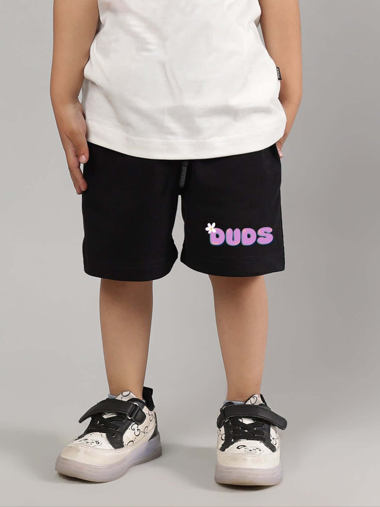 Child wearing NO POS black shorts from DUDS, featuring a playful logo design, suitable for both boys and girls.