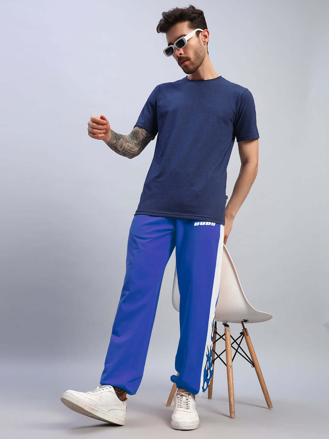 Man wearing BRACER RELAXED FIT JOGGERS BLUE-WHITE standing casually with chair in background.