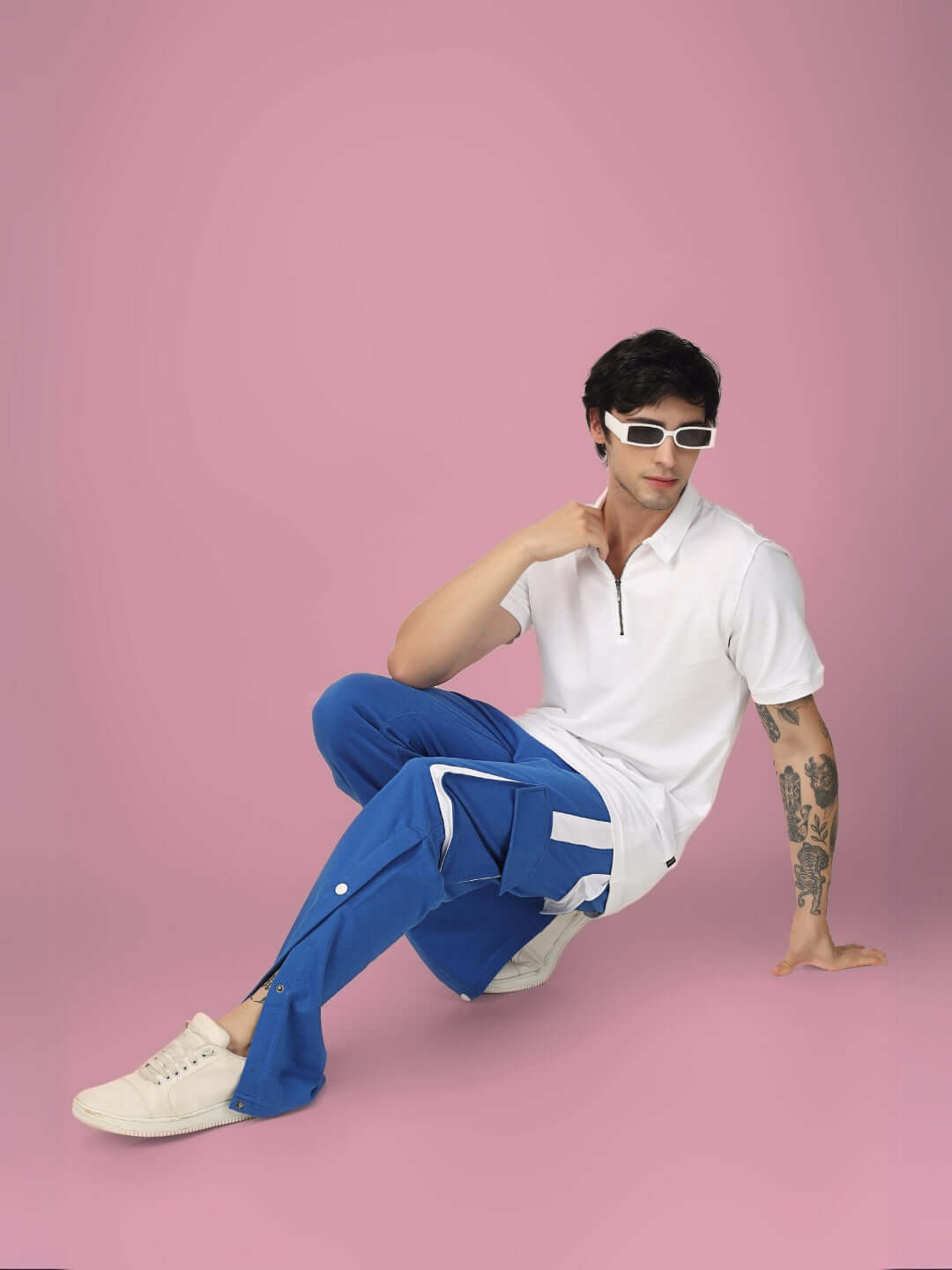 Model wearing blue and white BRACKET CARGO PANT with highlighter details, styled with a white shirt, seated against a pink background.